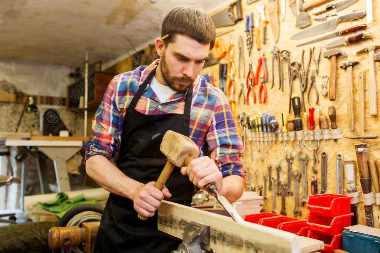 职业,木工,木制品和人们观念-木匠用锤子和凿子在车间加工木板